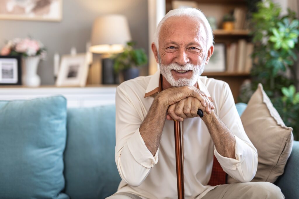 Implant-Supported Dentures Wauwatosa Older gentleman sitting on the couch holding his cane smiling.